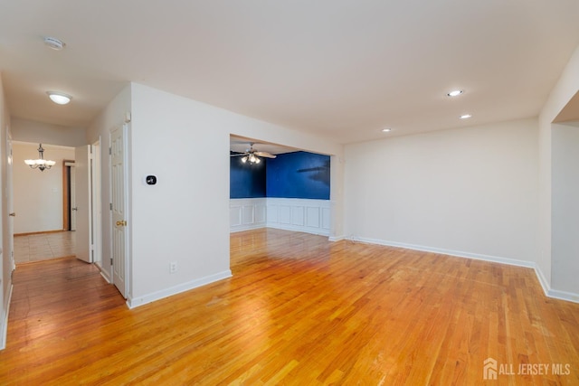 empty room with ceiling fan with notable chandelier and light hardwood / wood-style floors