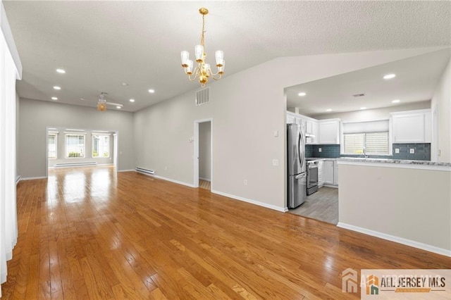 unfurnished living room featuring light wood-style flooring, visible vents, a wealth of natural light, and a chandelier