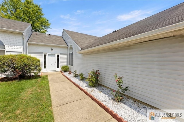 property entrance with a yard and roof with shingles