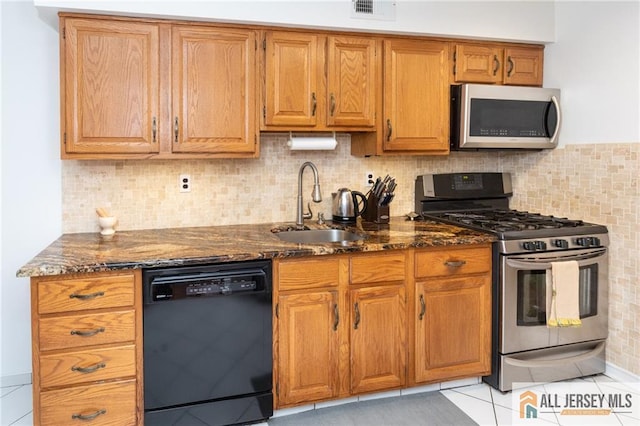 kitchen with light tile patterned flooring, appliances with stainless steel finishes, dark stone counters, and sink