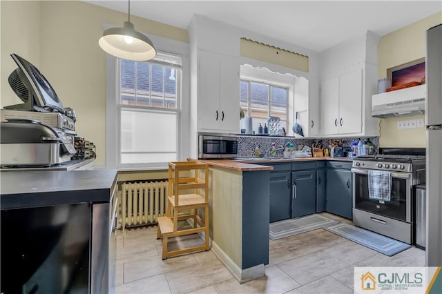 kitchen with light tile floors, white cabinets, appliances with stainless steel finishes, radiator, and backsplash