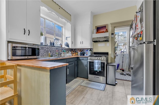 kitchen with light tile flooring, wooden counters, appliances with stainless steel finishes, gray cabinetry, and backsplash