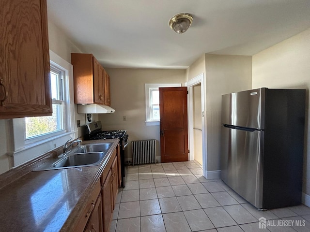 kitchen with radiator heating unit, appliances with stainless steel finishes, sink, plenty of natural light, and light tile patterned flooring