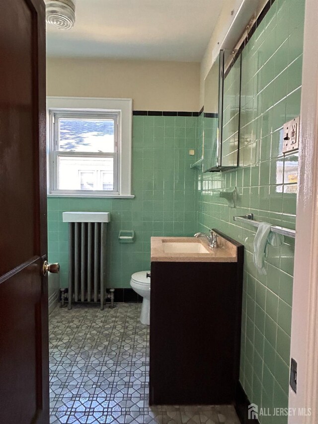 bathroom with tile walls, toilet, radiator heating unit, and vanity