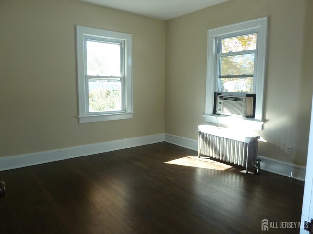 spare room with cooling unit, radiator, a wealth of natural light, and dark hardwood / wood-style flooring