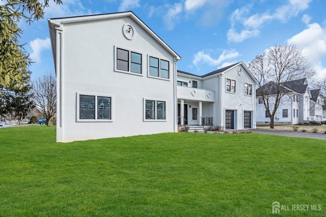 view of front facade featuring driveway, a balcony, a front lawn, and stucco siding