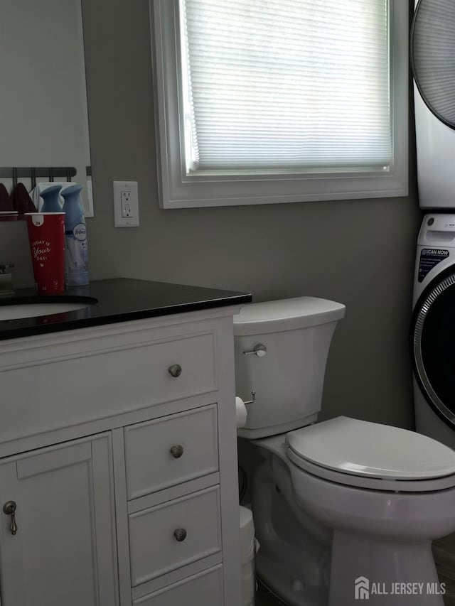 bathroom featuring toilet, vanity, and stacked washing maching and dryer