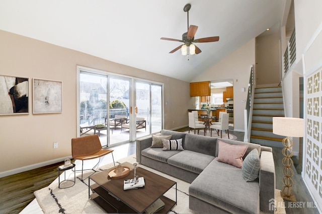 living room featuring stairway, a ceiling fan, wood finished floors, baseboards, and high vaulted ceiling