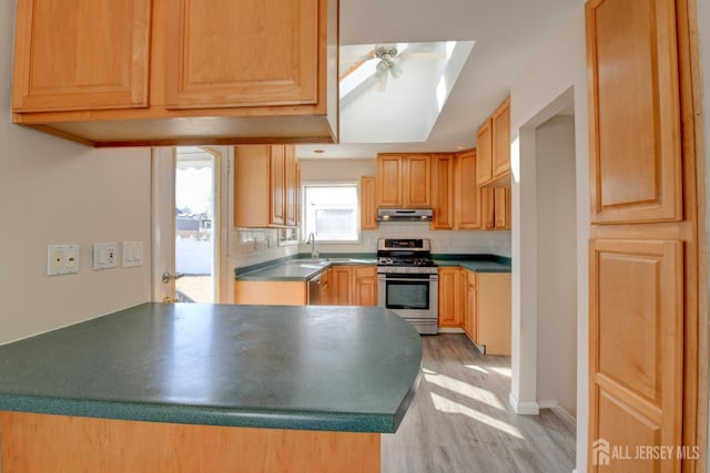 kitchen featuring light wood finished floors, ceiling fan, decorative backsplash, under cabinet range hood, and gas range