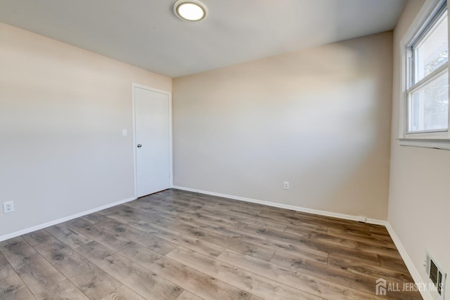 empty room featuring wood finished floors, visible vents, and baseboards