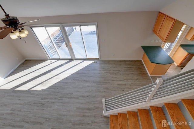 unfurnished living room featuring stairway, light wood-style floors, baseboards, and ceiling fan