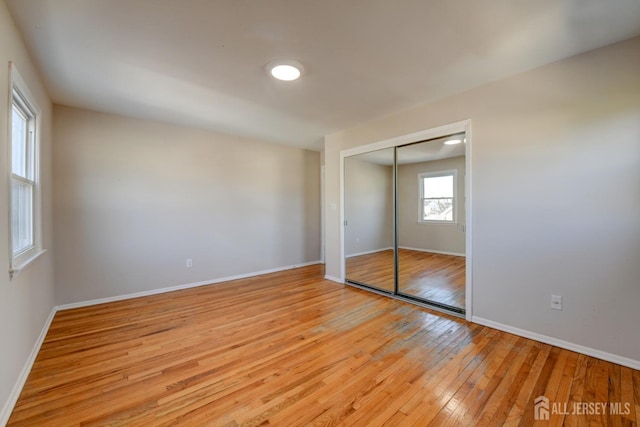 unfurnished bedroom featuring light wood finished floors, baseboards, and a closet