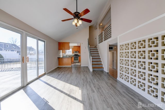 unfurnished living room featuring high vaulted ceiling, a ceiling fan, stairway, light wood finished floors, and baseboards