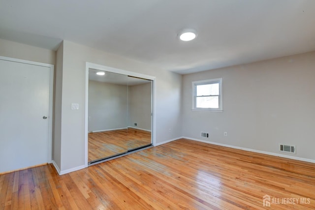 unfurnished bedroom featuring a closet, visible vents, baseboards, and hardwood / wood-style flooring