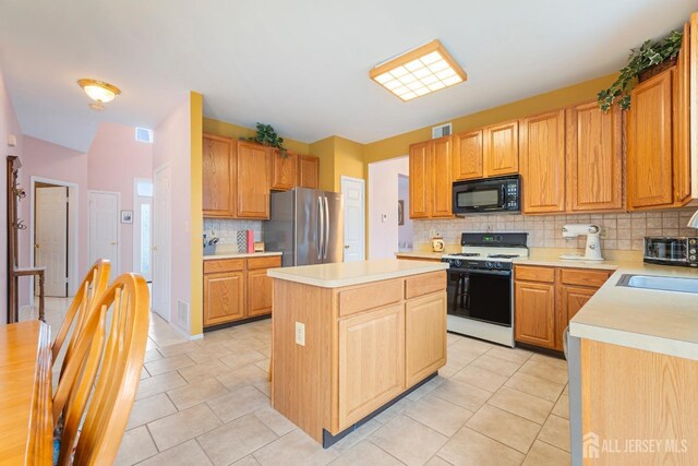 kitchen with light tile patterned flooring, backsplash, stainless steel fridge, white range with gas cooktop, and a kitchen island