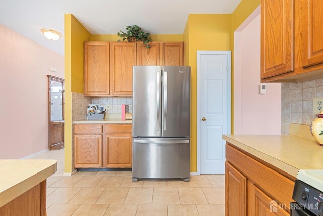 kitchen featuring light tile patterned floors, backsplash, and stainless steel refrigerator