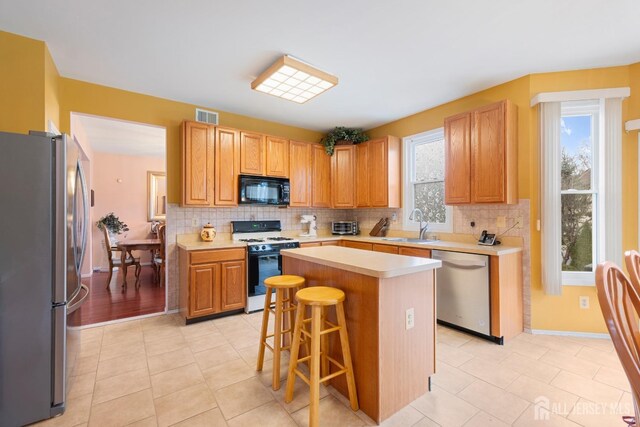 kitchen featuring sink, light tile patterned floors, appliances with stainless steel finishes, a kitchen island, and a kitchen bar