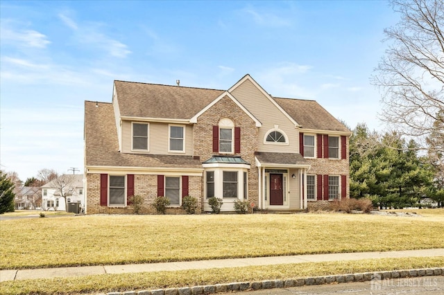 view of front of property with a front lawn, brick siding, and roof with shingles