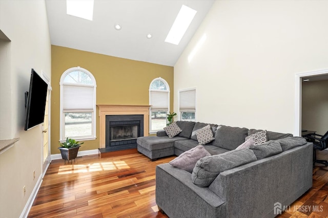 living area with light wood-type flooring, high vaulted ceiling, a fireplace with raised hearth, a skylight, and baseboards