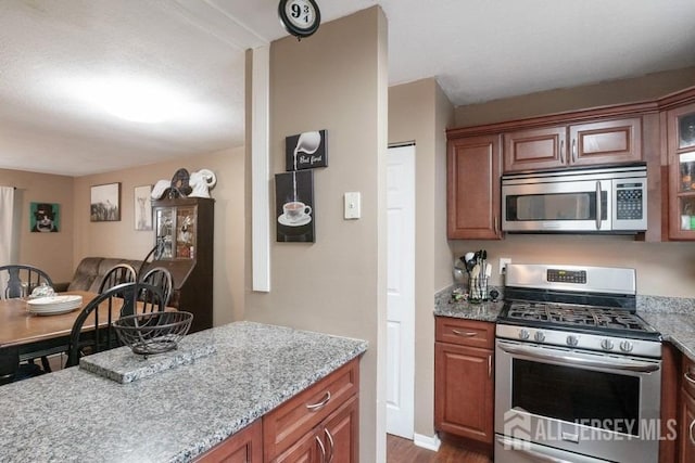 kitchen featuring light stone countertops, glass insert cabinets, stainless steel appliances, and brown cabinetry