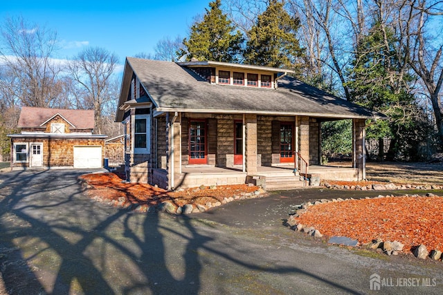 view of front of house with driveway, stone siding, a porch, and roof with shingles