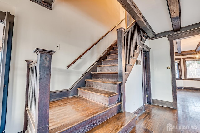 stairway with wood-type flooring, beamed ceiling, and baseboards