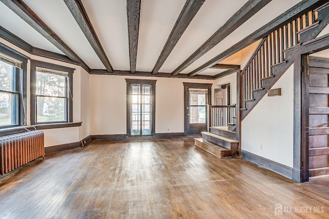 unfurnished living room featuring baseboards, radiator, wood-type flooring, stairs, and beam ceiling