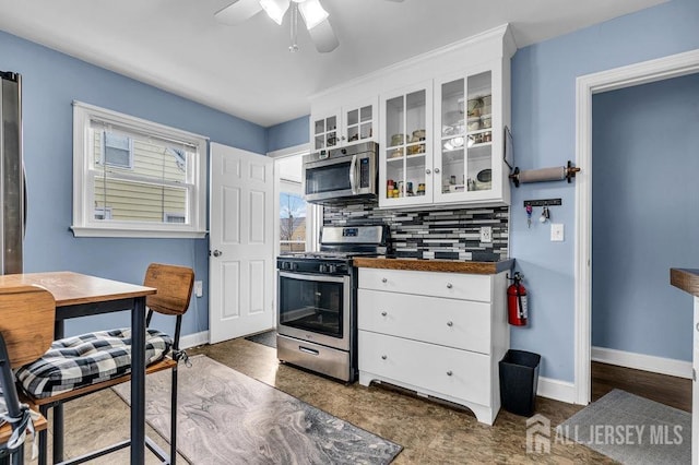 kitchen with decorative backsplash, baseboards, appliances with stainless steel finishes, and white cabinetry