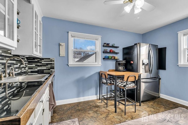 kitchen with baseboards, stainless steel fridge with ice dispenser, a sink, white cabinets, and tasteful backsplash