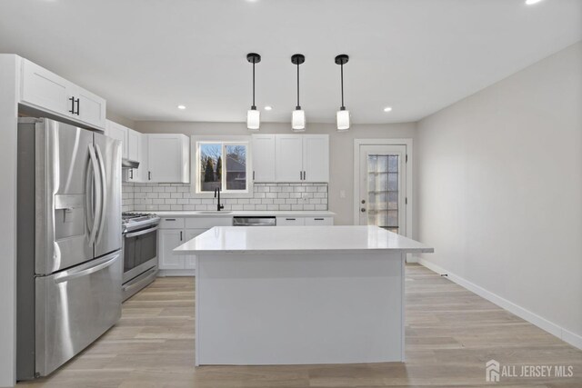 kitchen featuring white cabinets, appliances with stainless steel finishes, a center island, decorative backsplash, and hanging light fixtures