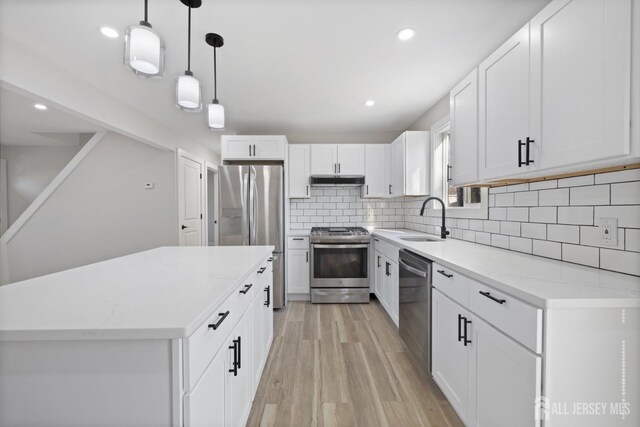 kitchen featuring appliances with stainless steel finishes, pendant lighting, white cabinets, light stone counters, and sink