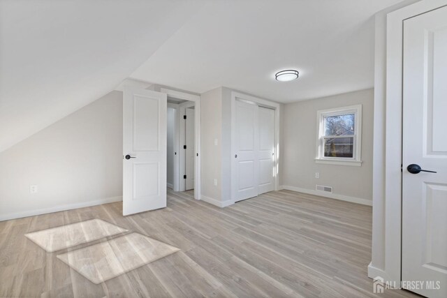 unfurnished bedroom with vaulted ceiling and light wood-type flooring