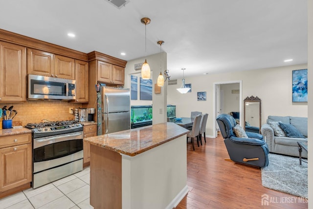 kitchen with backsplash, open floor plan, appliances with stainless steel finishes, light stone countertops, and hanging light fixtures