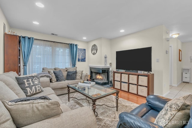 living area featuring visible vents, a warm lit fireplace, wood finished floors, recessed lighting, and baseboards