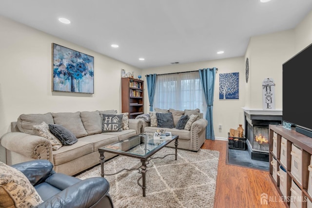 living area featuring wood finished floors, visible vents, baseboards, a fireplace with flush hearth, and recessed lighting