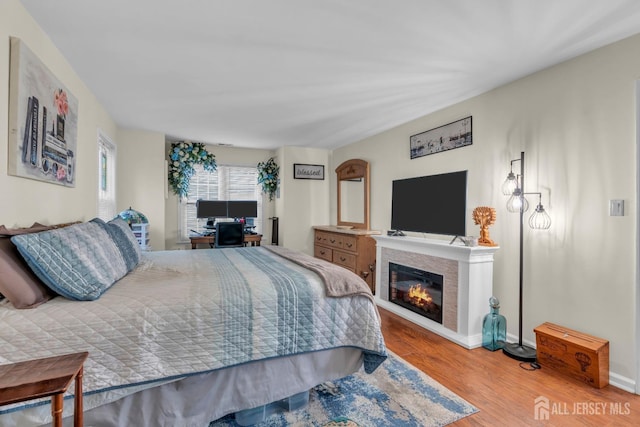 bedroom featuring a glass covered fireplace, baseboards, and wood finished floors