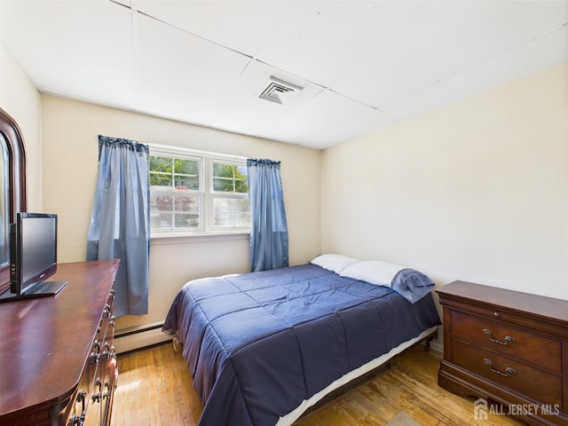bedroom featuring a baseboard heating unit, wood finished floors, and visible vents