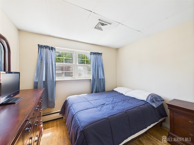 bedroom featuring wood finished floors, a baseboard heating unit, and visible vents