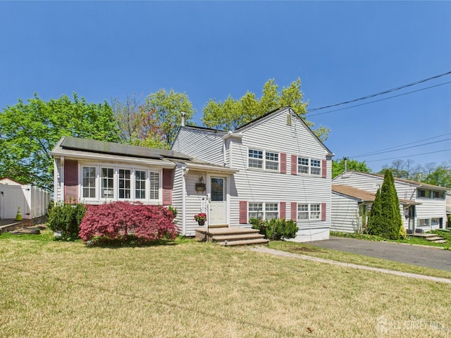 tri-level home with aphalt driveway, fence, a front yard, and solar panels