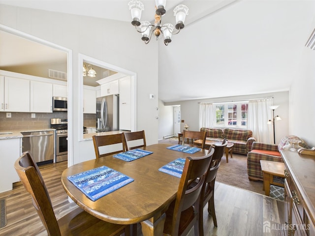 dining room with visible vents, an inviting chandelier, wood finished floors, and vaulted ceiling