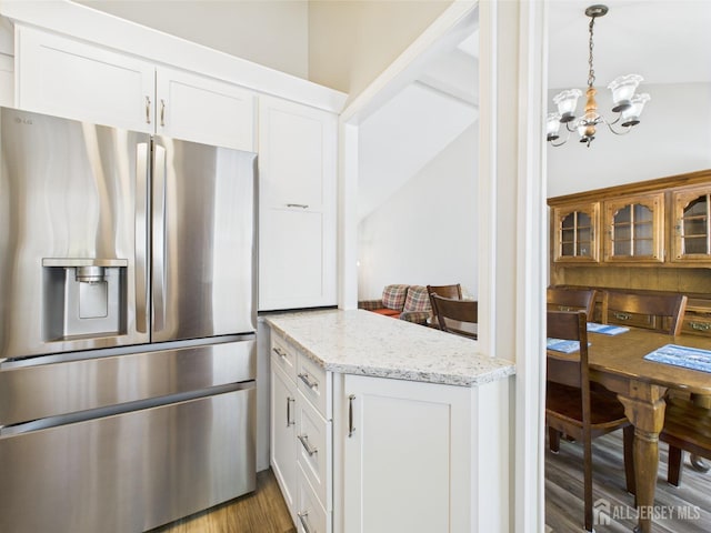 kitchen with stainless steel fridge, white cabinets, wood finished floors, and a chandelier