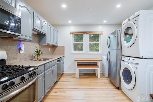 interior space with stacked washer / drying machine, sink, light hardwood / wood-style flooring, decorative backsplash, and stainless steel appliances