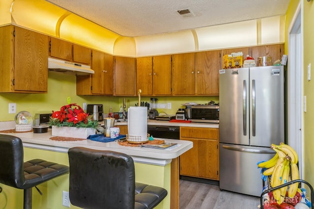114 Griggs Pl E, Brunswick, NJ 08816 - kitchen with stainless steel appliances, under cabinet range hood, light countertops, light wood finished floors, and brown cabinetry