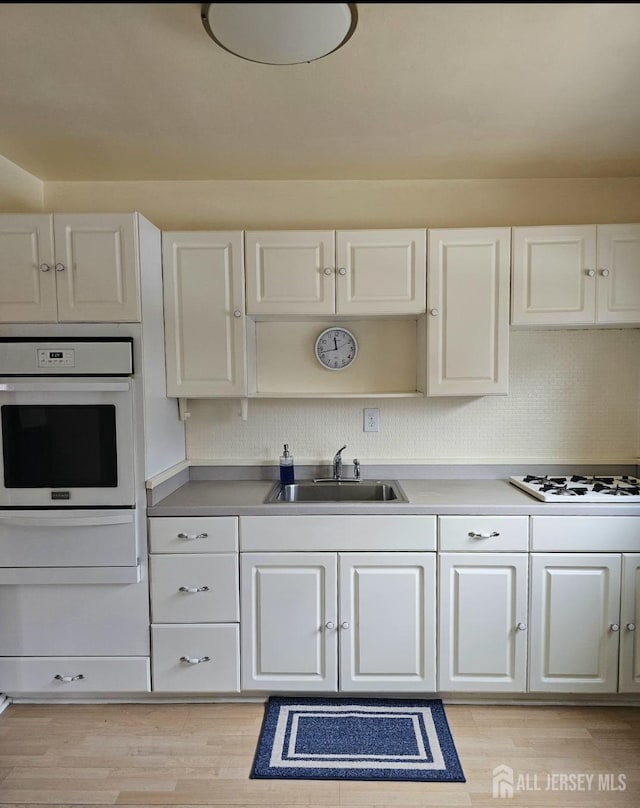 kitchen featuring a warming drawer, light wood-type flooring, a sink, white appliances, and white cabinets