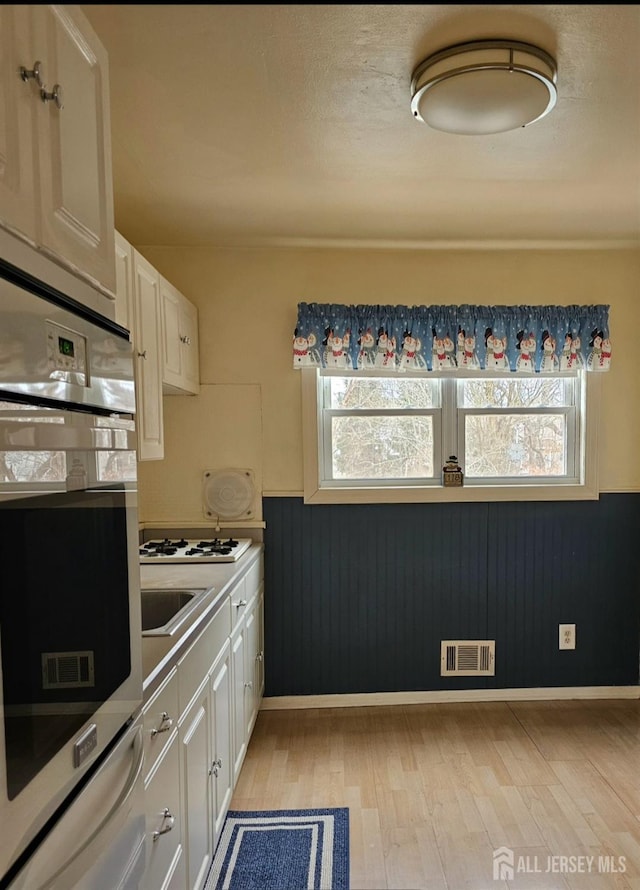 kitchen with stainless steel oven, a healthy amount of sunlight, and white cabinetry