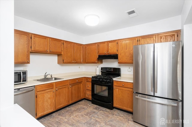 kitchen featuring appliances with stainless steel finishes, brown cabinetry, a sink, and under cabinet range hood