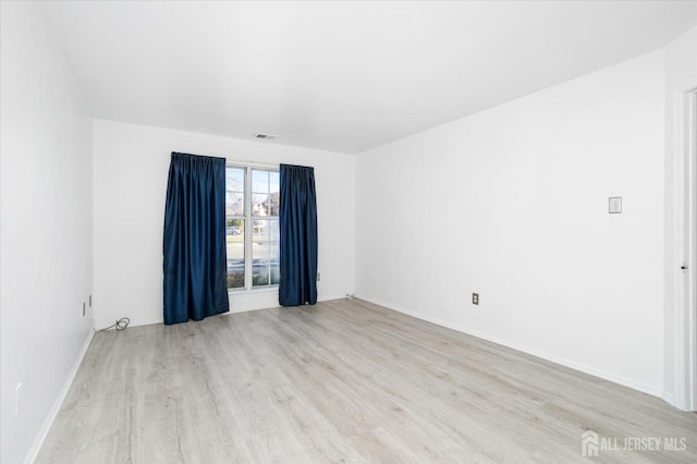 spare room with baseboards, visible vents, and wood finished floors