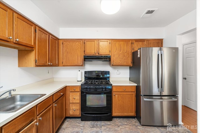 kitchen featuring black gas range, a sink, visible vents, freestanding refrigerator, and range hood