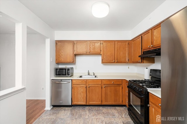 kitchen with brown cabinets, light countertops, appliances with stainless steel finishes, a sink, and under cabinet range hood