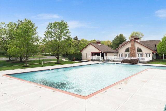 community pool with a patio area, fence, and a yard